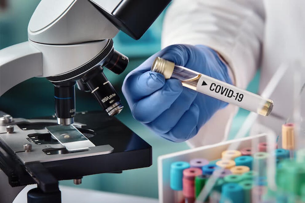 A medical researcher examining a vial with the word "COVID-19" on it