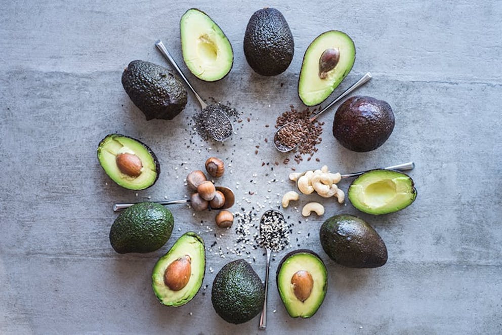 Fresh avocado halves arranged in circle on table with nuts and seeds, healthy fats, good fats.