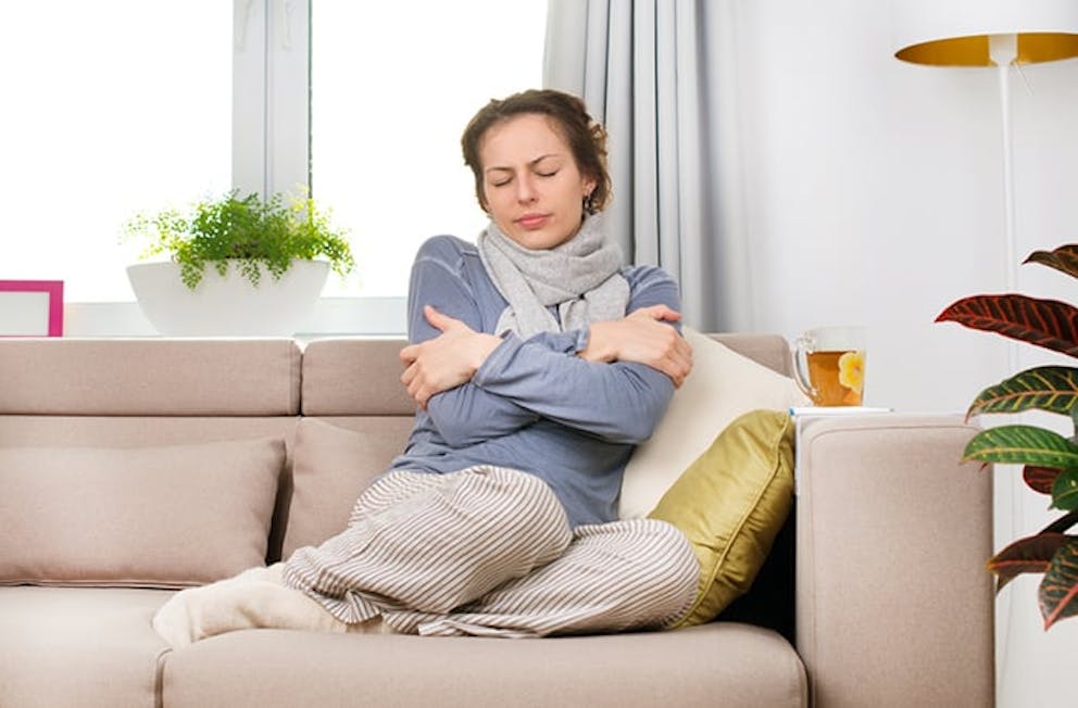 Sick woman on couch with flu-like symptoms like fever, aches, fatigue, cold.