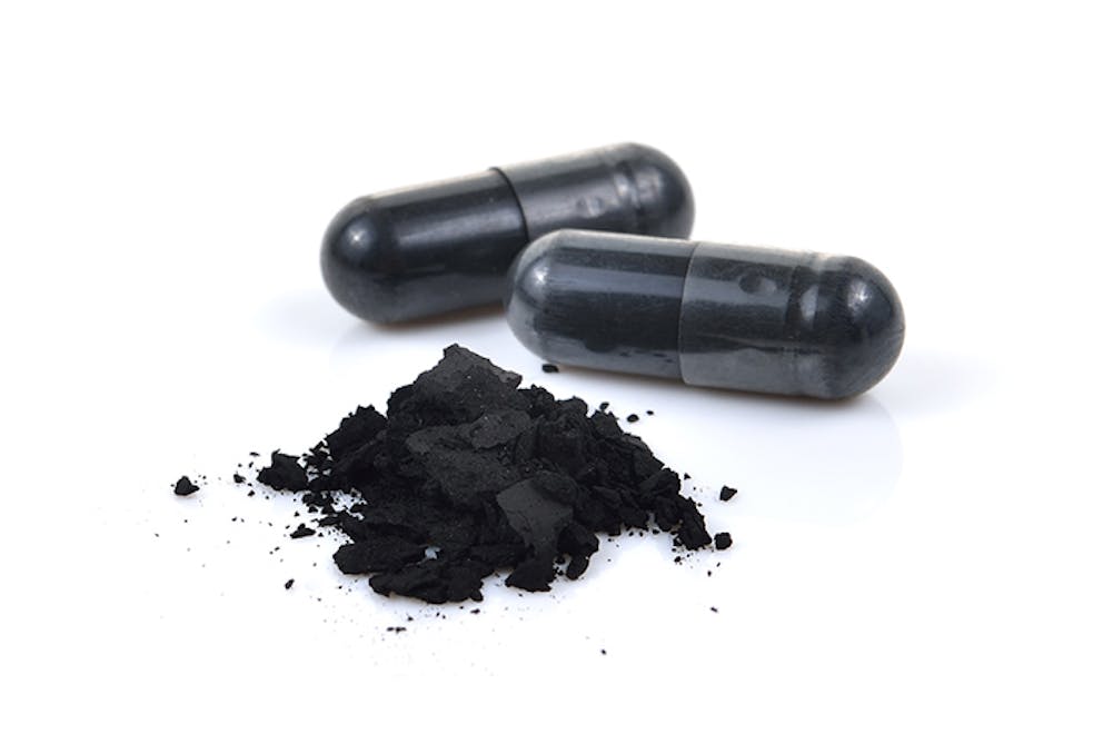 Black activated charcoal powder and capsules supplement on white background.