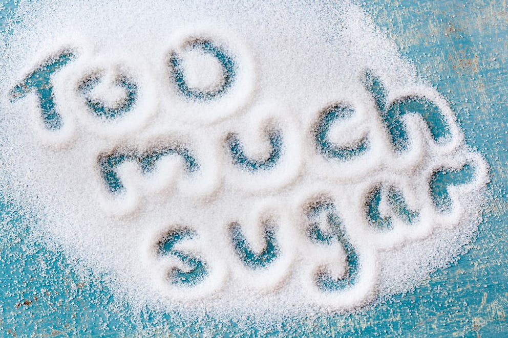 The words too muchsugar written in a pile of sugar grains on blue table.
