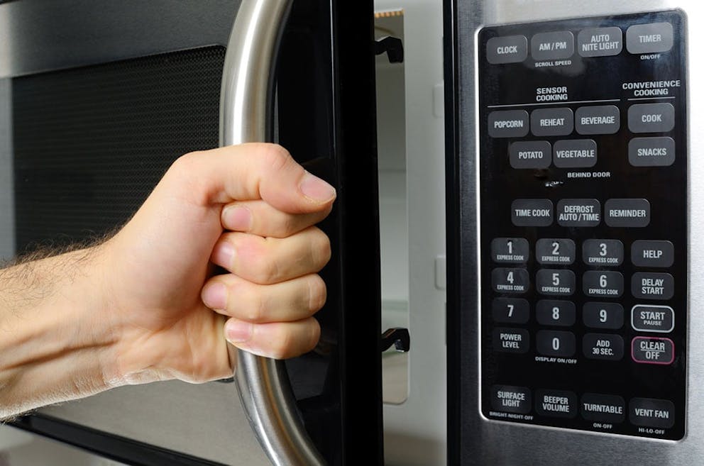 Man’s hand on microwave door handle, microwave keypad cooking time for heating food.