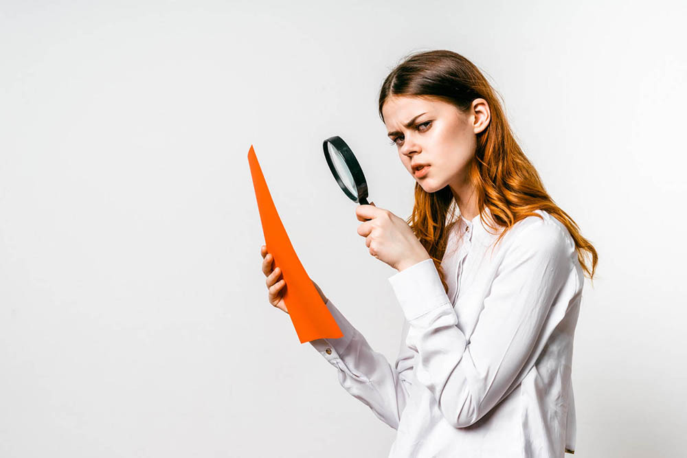 A young woman inspects an orange research paper with a magnifying glass | skipping breakfast and weight gain