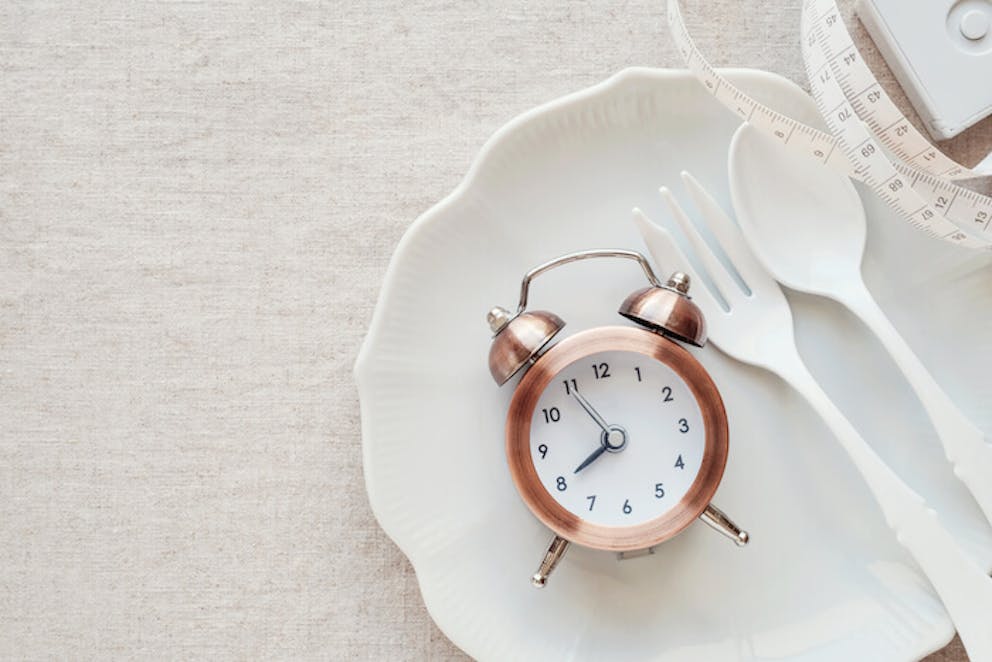 A small clock sitting on a plate next to cutlery and a measuring tape | Dr. Jason Fung MD and Intermittent Fasting