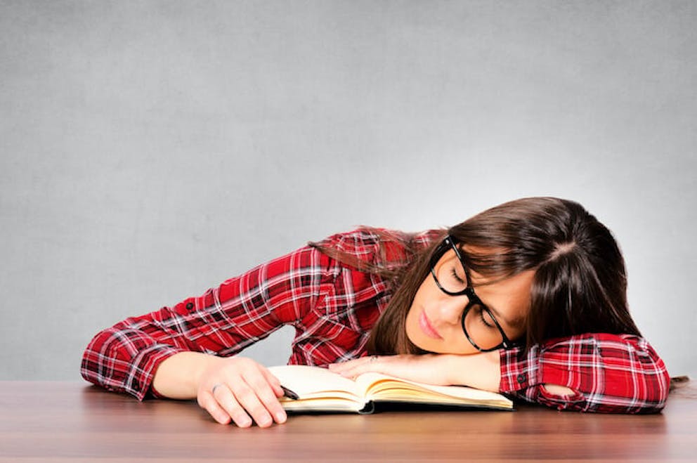 Woman exhausted and sleeping on a desk with a book | Eat More Magnesium Foods, and You'll Feel a Lot Better