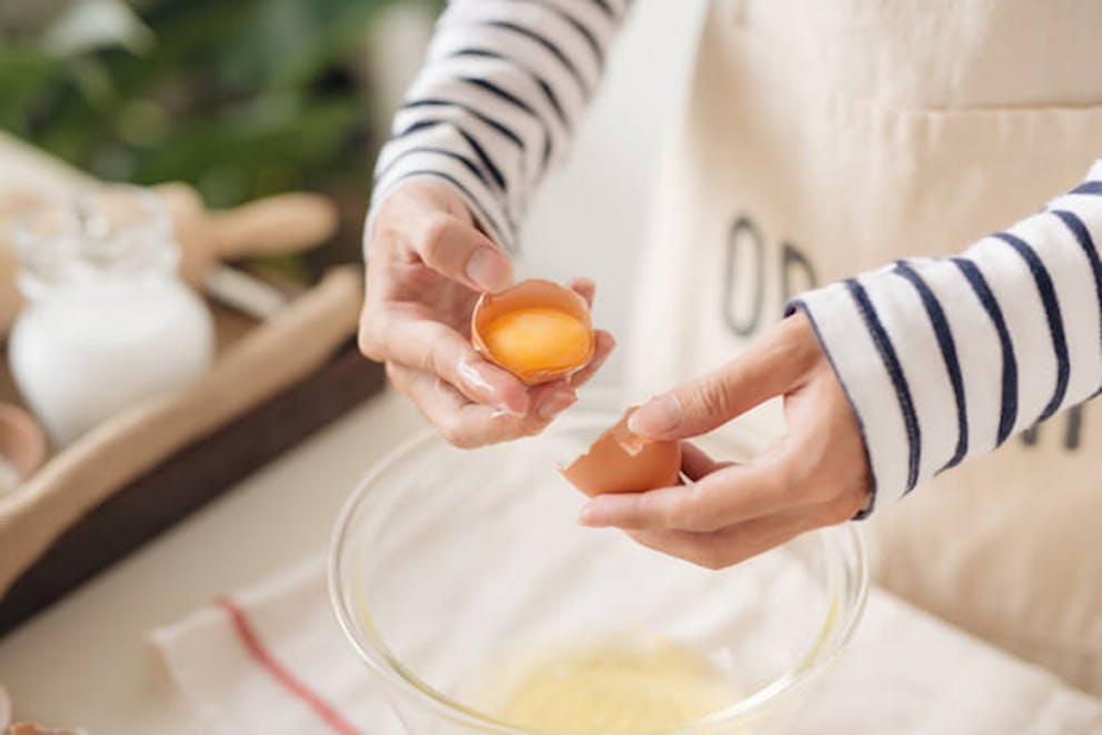 A woman in a kitchen separating an egg yolk from an egg white.  | Egg Yolk vs. Egg White: Whats’ the Difference?