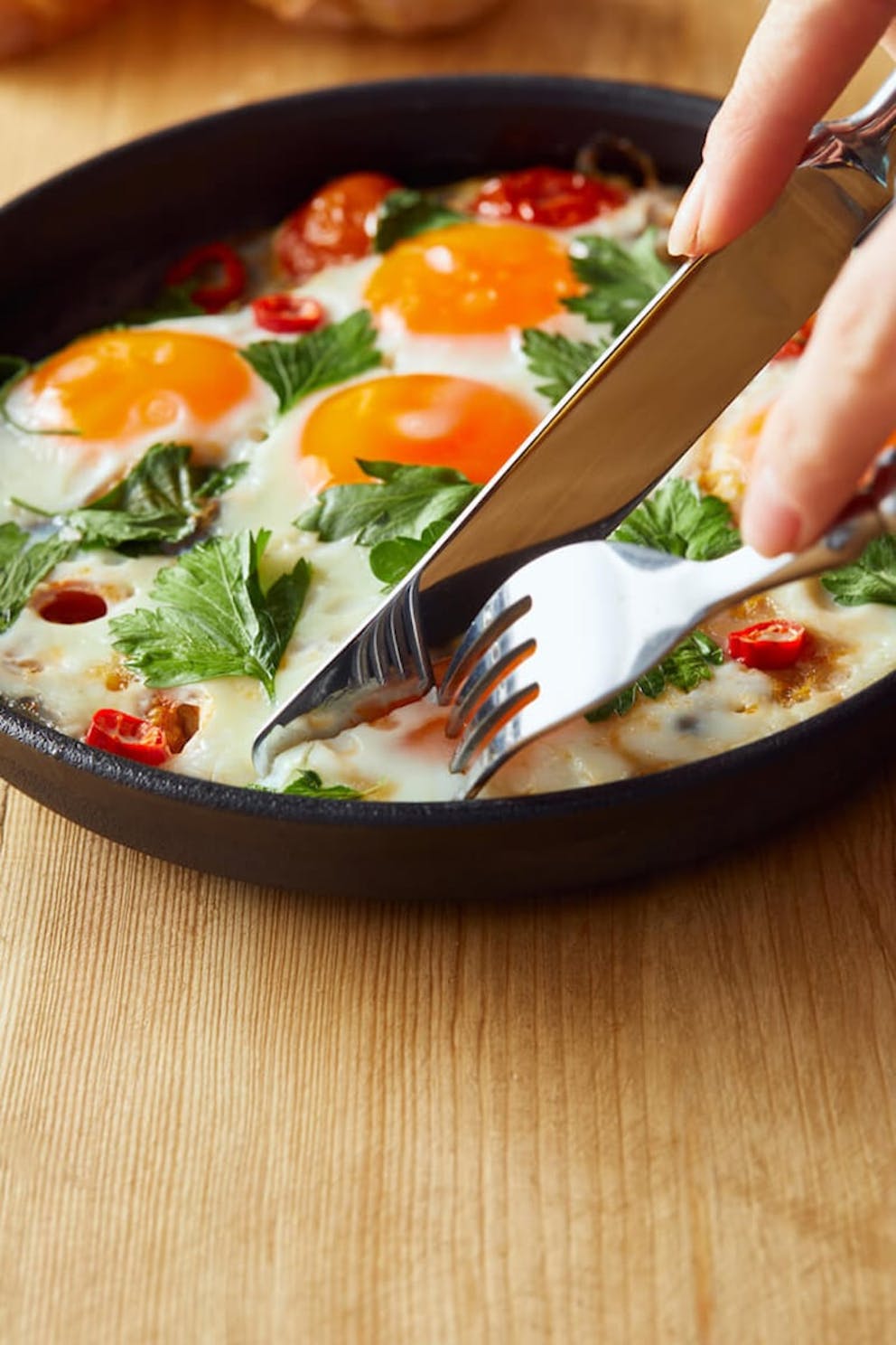 A person eating fried eggs with parsley and chili peppers on a wooden table with fork and knife. | Egg Yolk vs. Egg White: What’s the Difference?