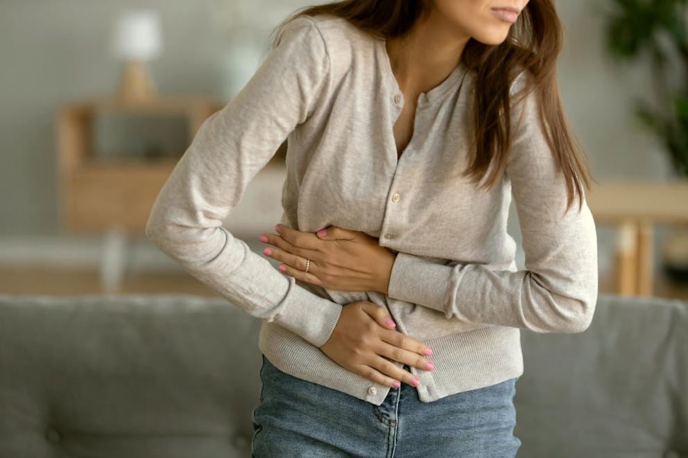 Young sick woman standing holding belly suffering from stomach pain  | Two Causes Of Eye Twitching, Especially Under The Left Eyelid | cause of eye twitching