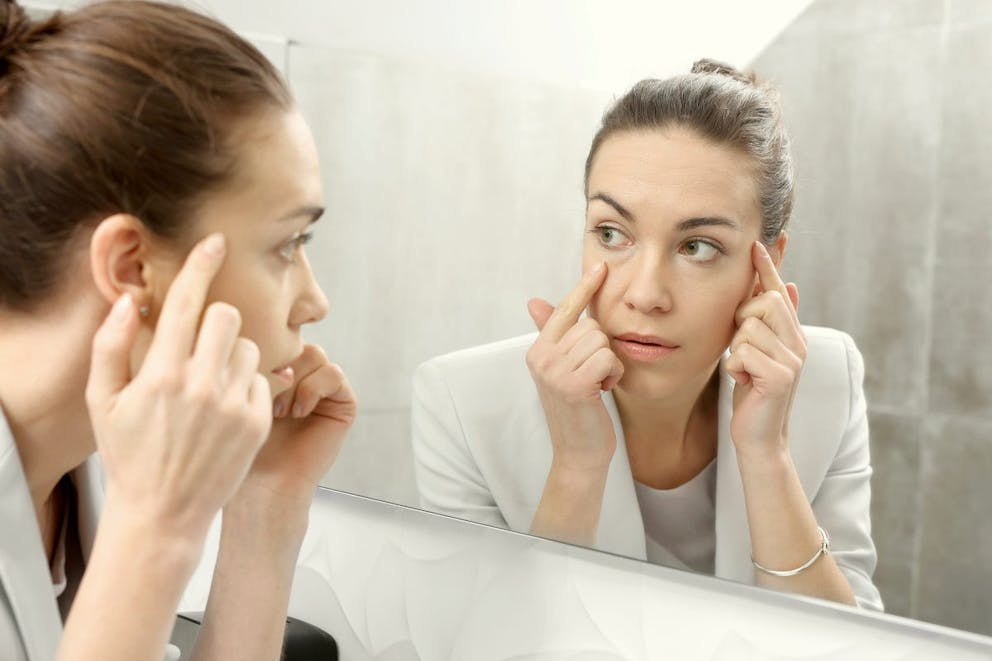 Woman looks in the mirror | Two Causes Of Eye Twitching, Especially Under The Left Eyelid | when to worry about eye twitching