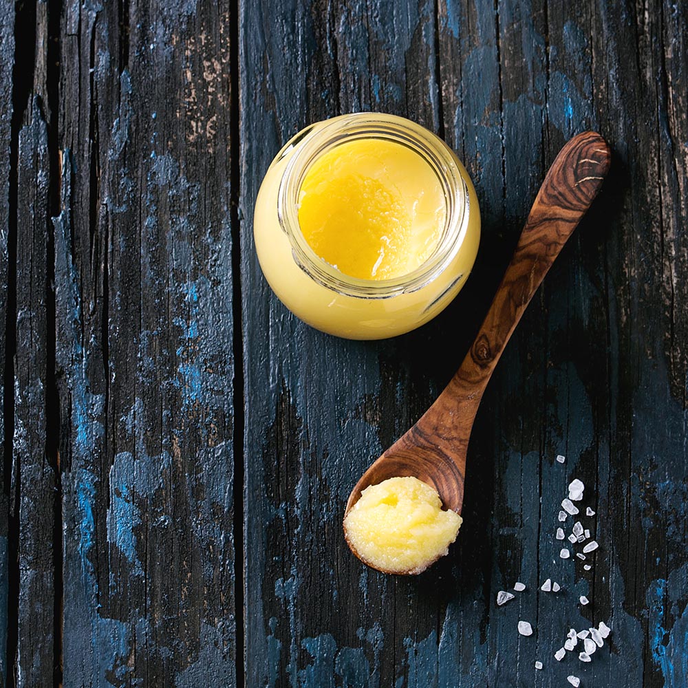 a clear glass pot of ghee with a wooden spoon containing ghee | Ghee Benefits on Health