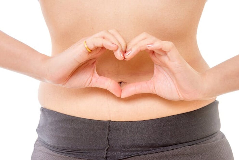 A woman making a heart with her hands and holding them in front of her bare stomach. 