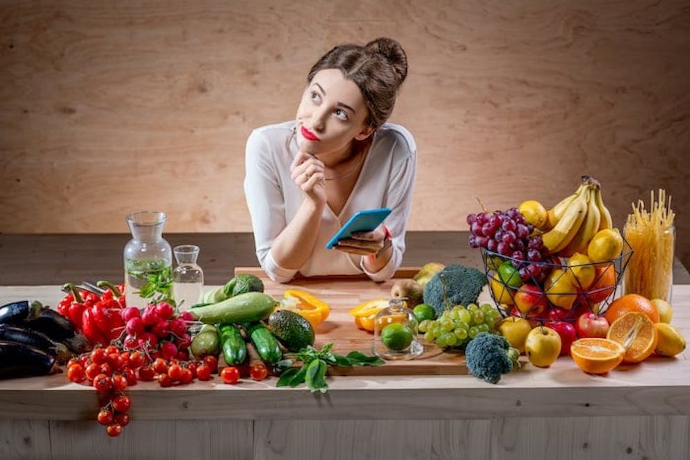 Woman counting calories with smartphone app while surrounded by healthy keto foods