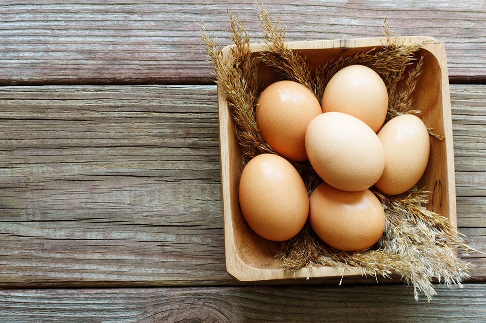 a wooden bowl full of brown eggs