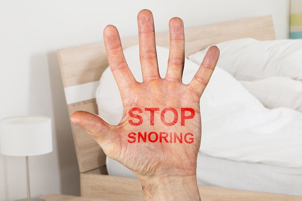 A hand held up with words STOP SNORING written in red with bedroom in the background.