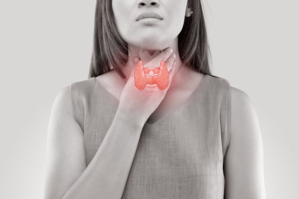 Woman in black and white holding hand to throat, thyroid gland drawn in red.
