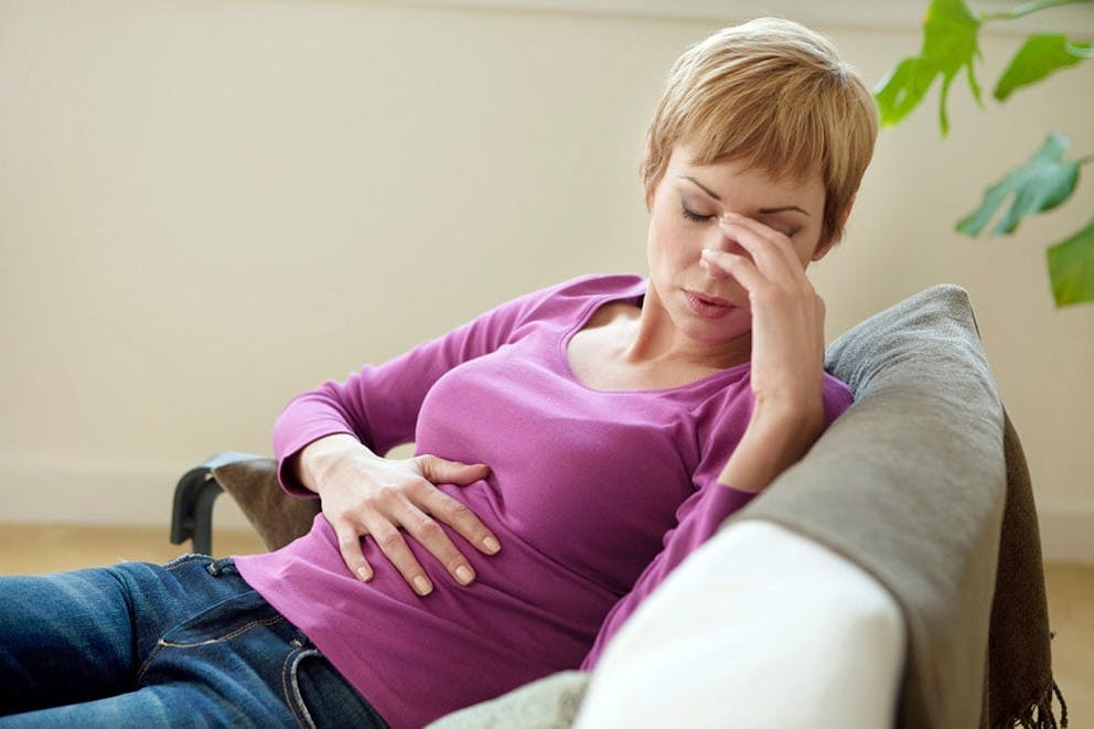 Woman in purple shirt on couch with abdominal pain and headache, arsenic poisoning symptoms.