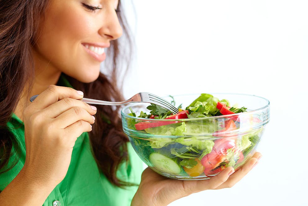 picture of a smiling healthy woman eating a large salad