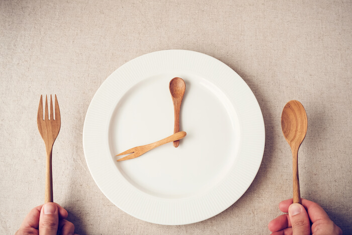 A person holding a wooden fork and spoon over an empty plate that looks like a clock.