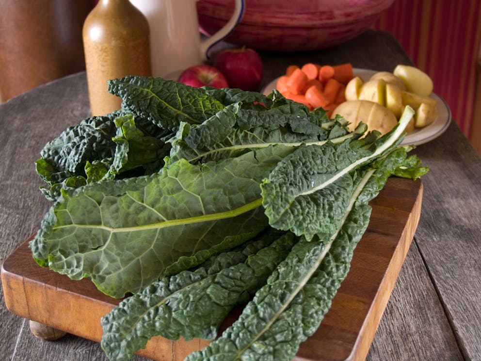 A bunch of dinosaur Lacinato kale on a wooden cutting board on kitchen table.