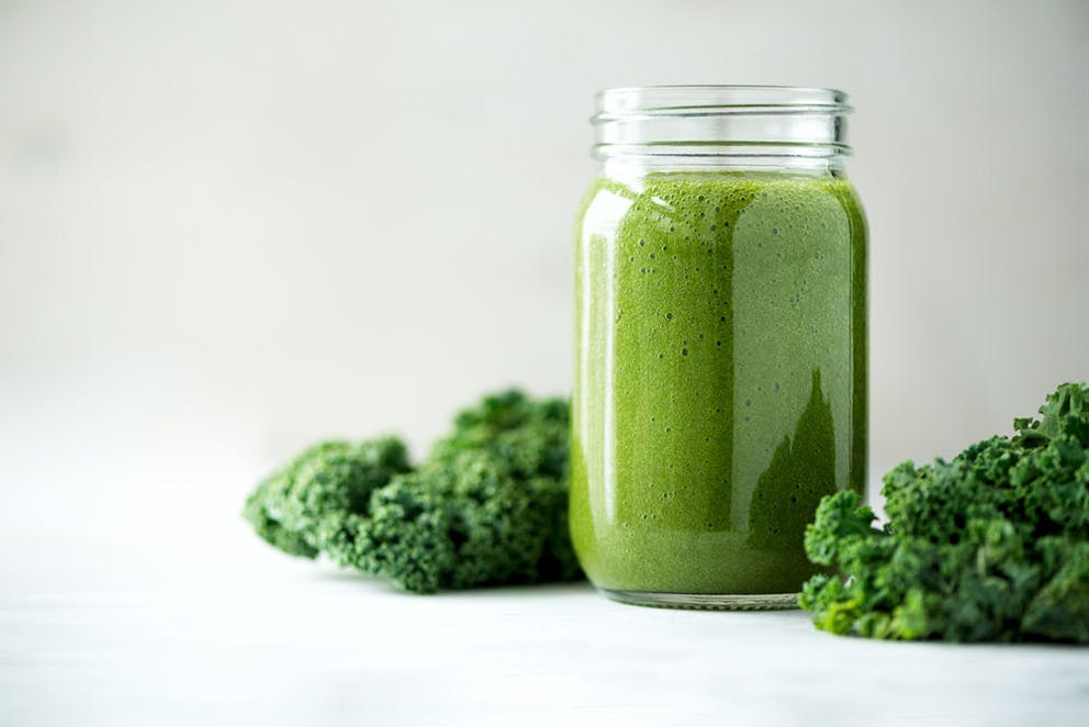 Glass mason jar full of green kale shake smoothie, with fresh raw kale next to it.