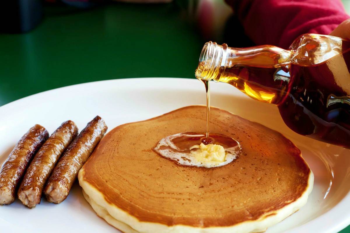 Bottle maple syrup being poured on pancake with three sausages | Keto-Friendly Maple Syrup Recipe
