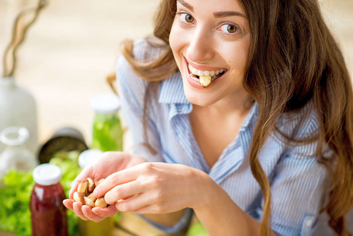 Closeup view from above of a woman eating brasil nuts with healthy food on the background | The Best Ketogenic Diet Foods To Eat