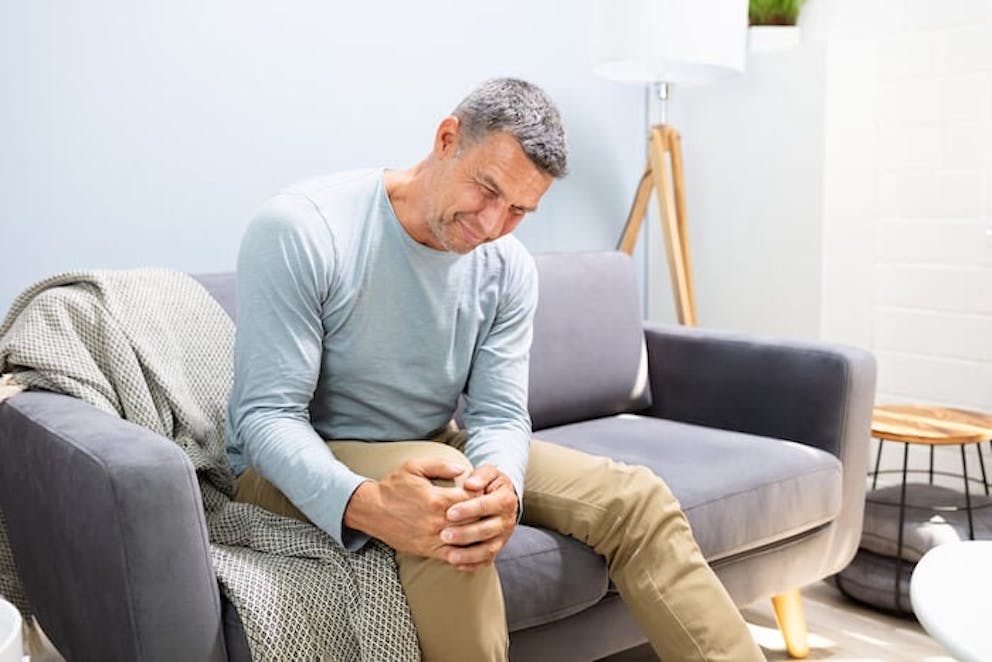 Man sitting on a couch holding knee with both hands | Amazing Knee Pain Relief Techniques