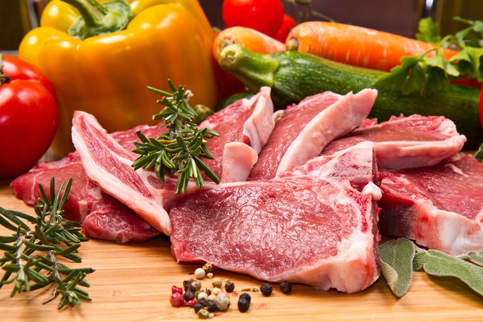 Pieces of red meat next to fresh vegetables and spices, protein and veggies.