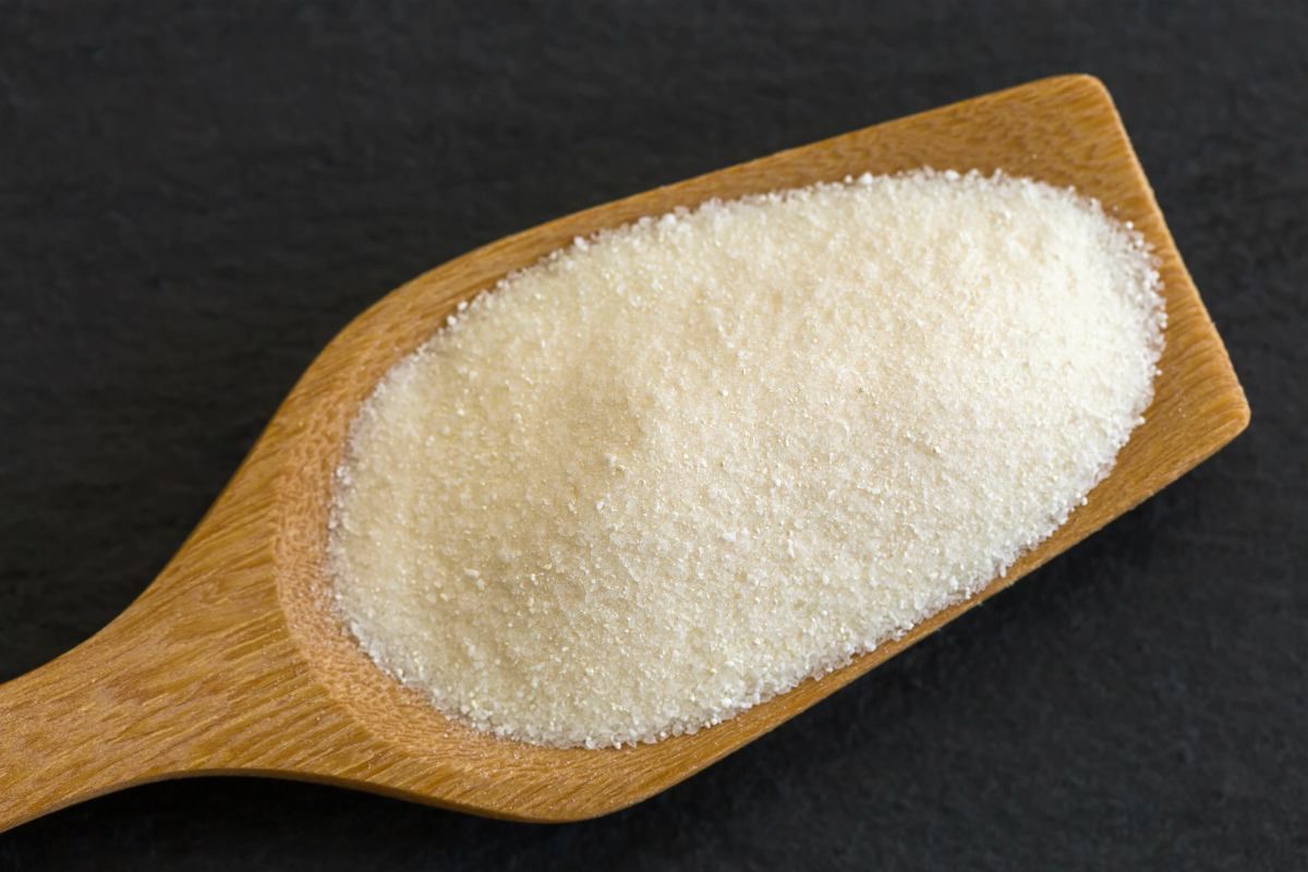 Wooden spoon full of dried white fine powder starch on dark stone background | Maltodextrin One Of The Worst Hidden Sugars