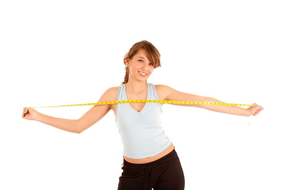A young happy woman stretches measuring tape with arms, healthy weight loss success