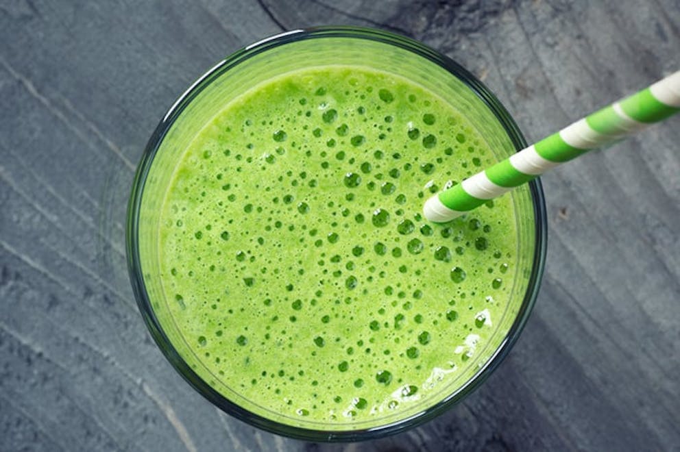 Top down view of kale shake, green smoothie in glass with striped green straw on wood table