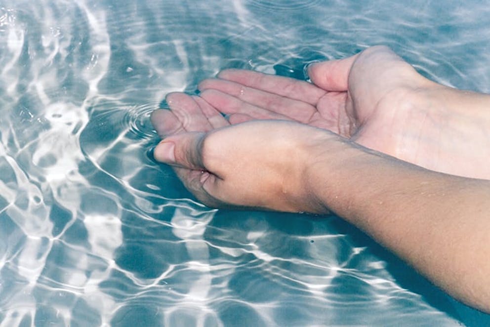 Hands in clear water, palms up submerged in water.