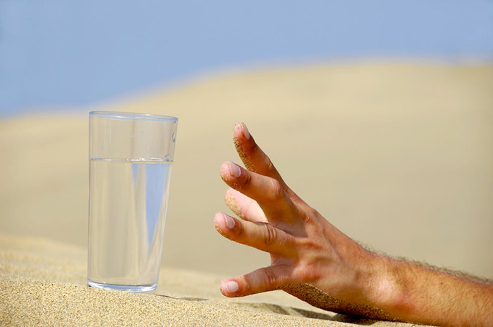 - Hand in sand reaching for clear glass of clean water – thirsty, how long without water.