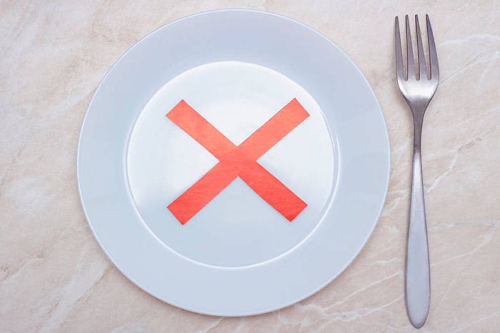 Empty white plate and silverware with no food, red X on plate – food restriction, fasting concept.