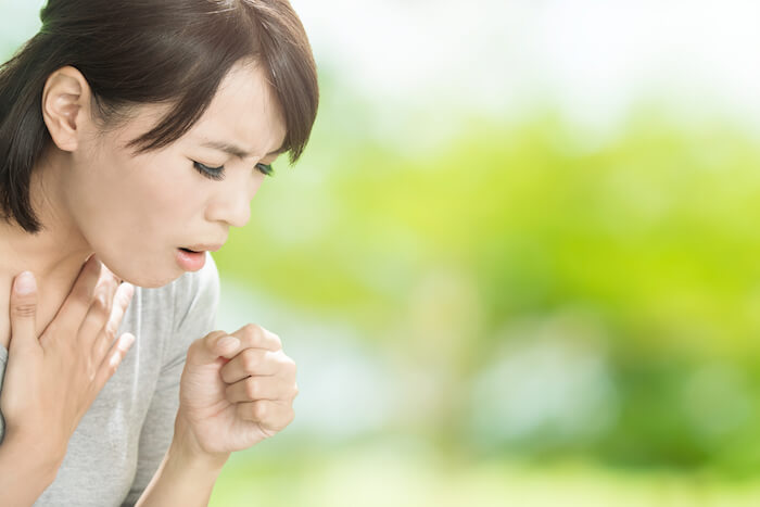 Woman with asthma coughing outside amongst green trees. |  Natural Remedies for Asthma