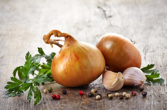 Two yellow onions sitting on a wood table next to garlic cloves | Natural Remedies for Lyme Disease