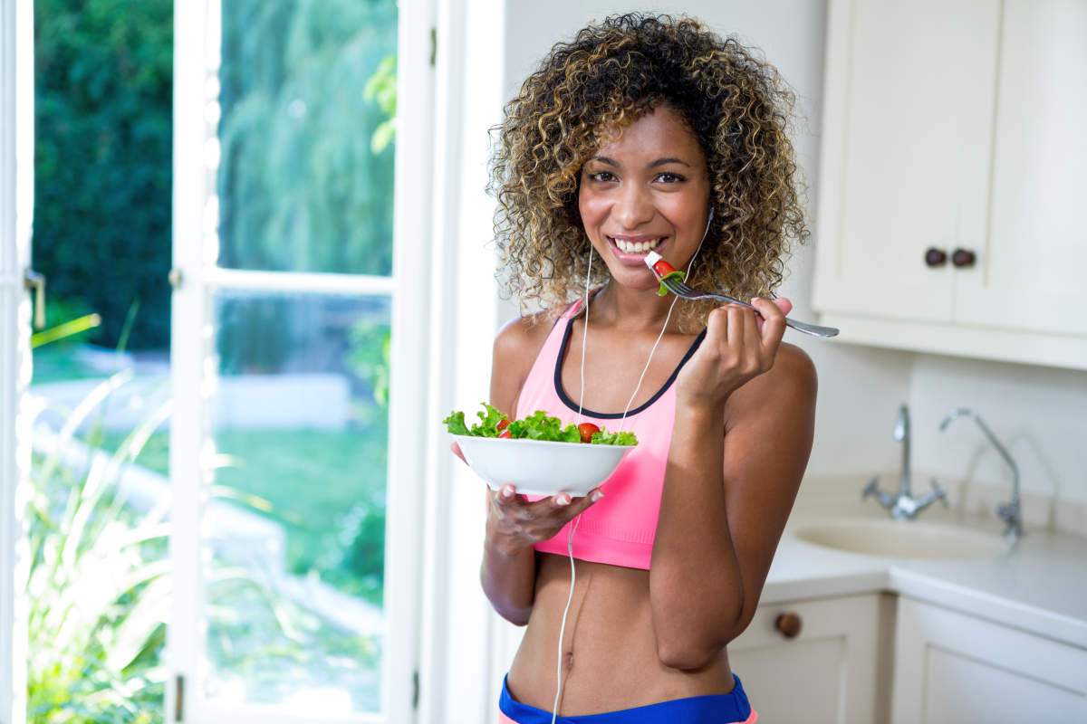 Portrait of woman having bowl of salad while listening to music in kitchen | The Importance of the NO CARB SNACKS Rule if You Want Weight Loss