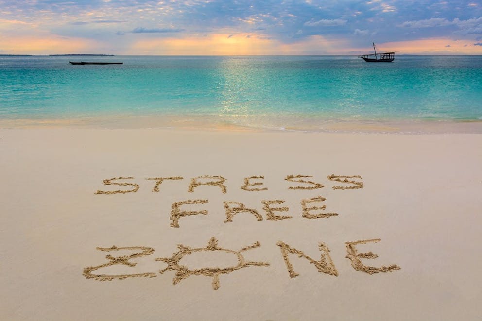 Beach at sunset, with words “stress free zone” written into the sand. No stress, stress relief.