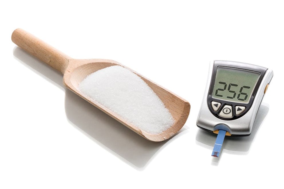 Wooden scoop of sugar next to blood sugar monitor, blood sugar spike unhealthy foods.