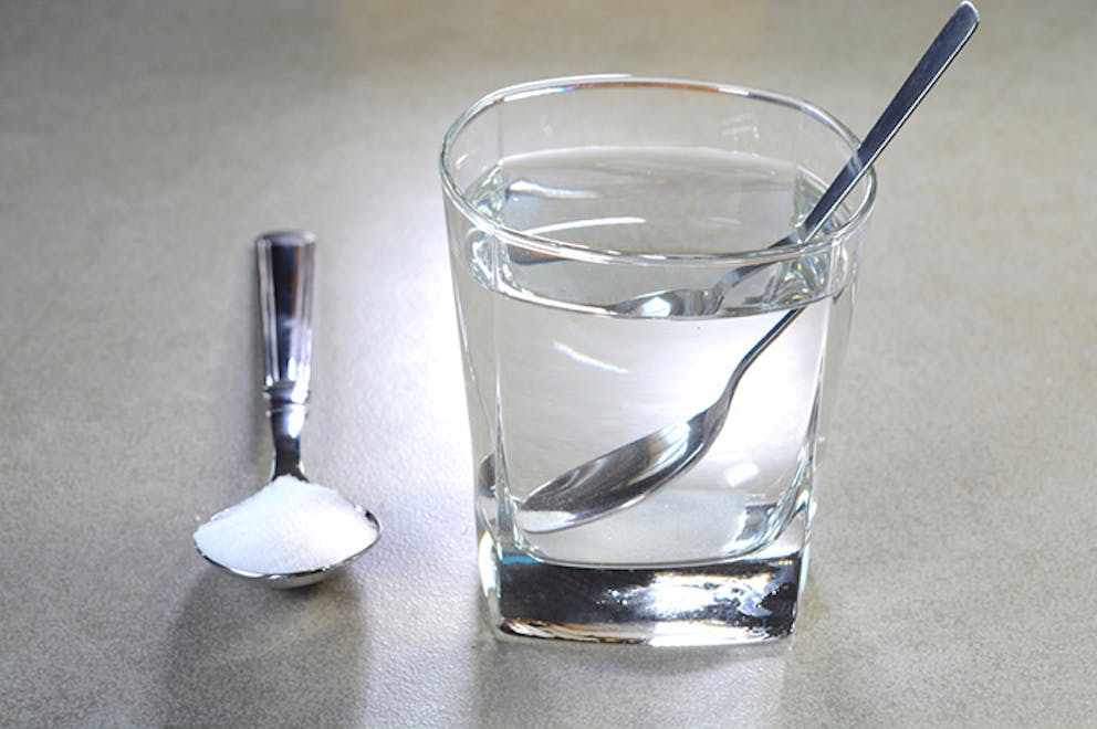 Glass cup of water with spoon, spoon of salt next to it, how to do a salt water gargle.