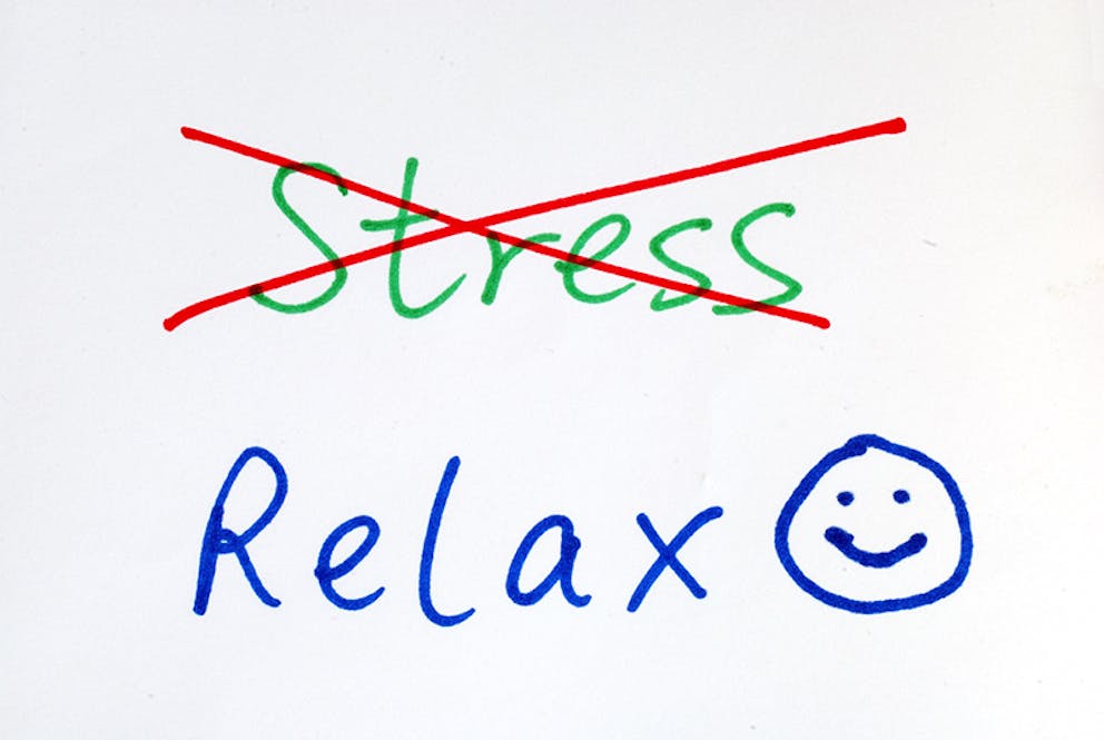 Piece of paper with stress crossed out and relax with a smiley face, no stress, relax more concept.