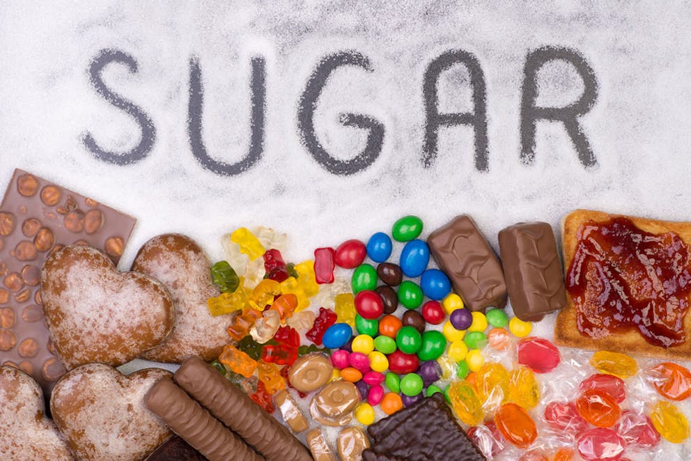 Unhealthy sugar types, candy, desserts, chocolates, with sugar written in sugar grains on table.