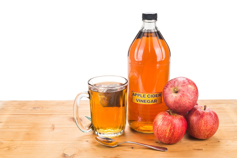 a picture of a bottle of apple cider vinegar with apples next to it