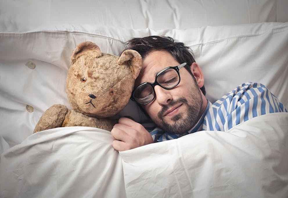 A man holding a teddy bear in bed sleeping like a baby.
