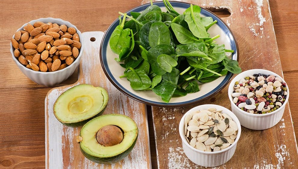 Magnesium-rich foods on wooden cutting boards – spinach, almonds, avocado, pumpkin seeds.