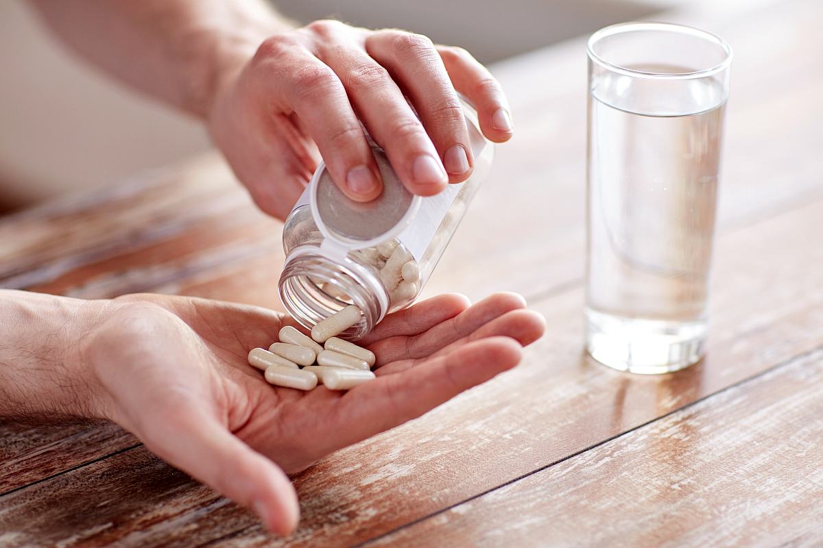 Close up of man with glass of water pouring pills from jar to hand | Symptoms of Low Electrolytes and How to Debug Them 