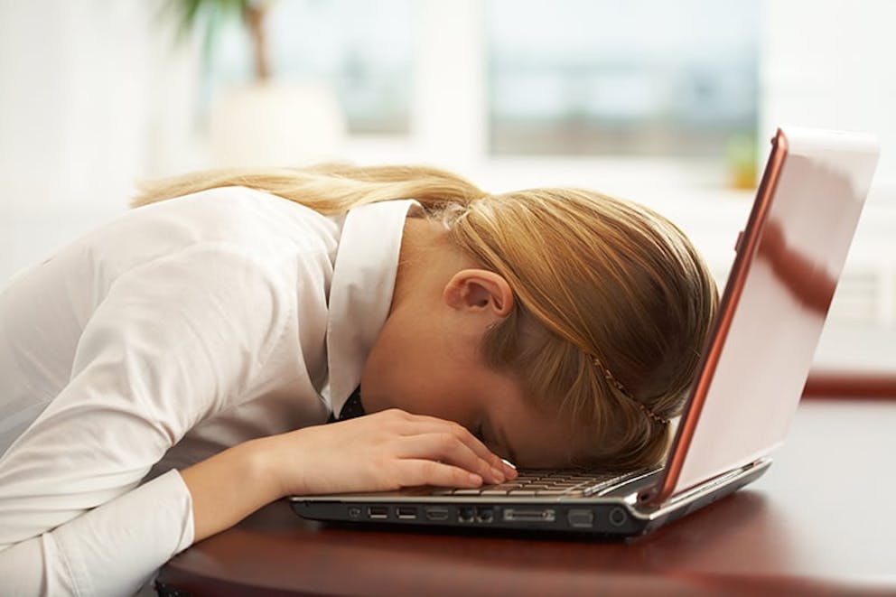 exhausted woman slumped over her laptop