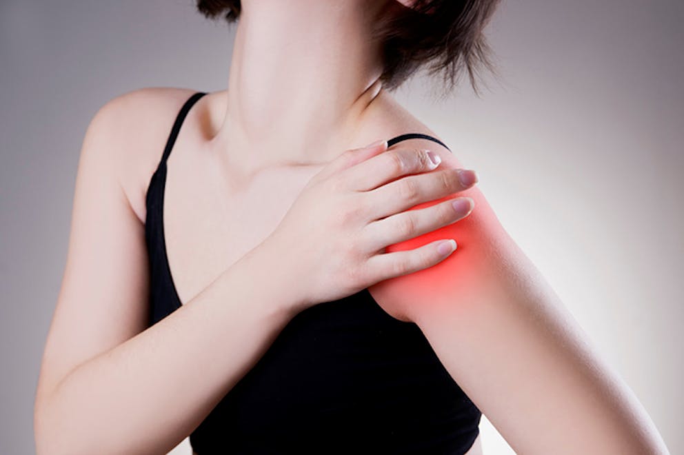 Young woman with shoulder pain holds her hand to her shoulder, red showing pain and inflammation.