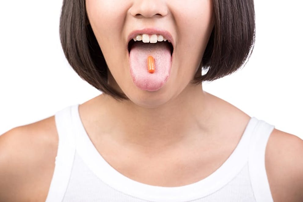Young woman in white tank top sticks out her tongue, taking a dietary supplement.