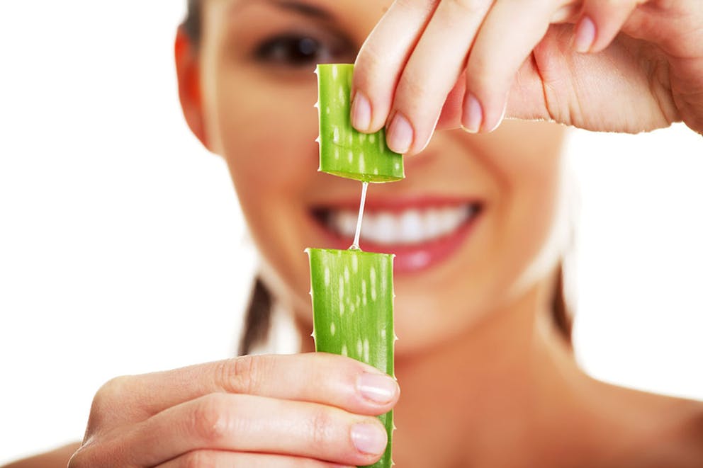 A smiling woman holds a piece of aloe cut in half with aloe vera gel, medicinal plant.
